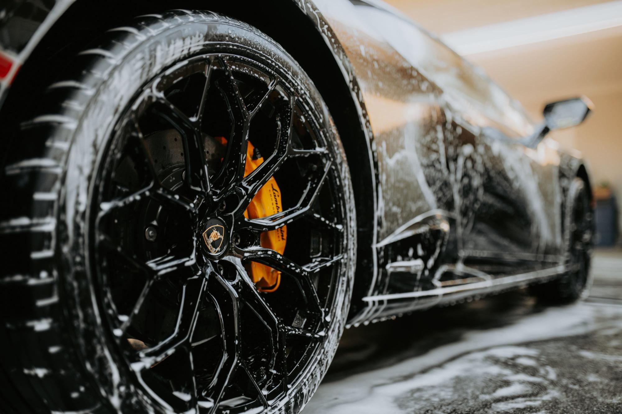 Close-up of a supercar wheel being washed with foam during detailing